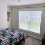 Bedroom with large window, bed, and dresser