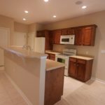 Galley kitchen with wood-tone cabinets, white appliances, and breakfast bar