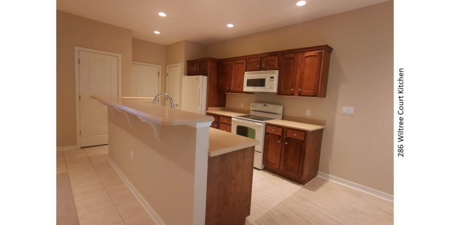 Galley kitchen with wood-tone cabinets, white appliances, and breakfast bar