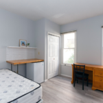 Room with bed, mini-fridge, counter, shelf, desk with chair, and dresser