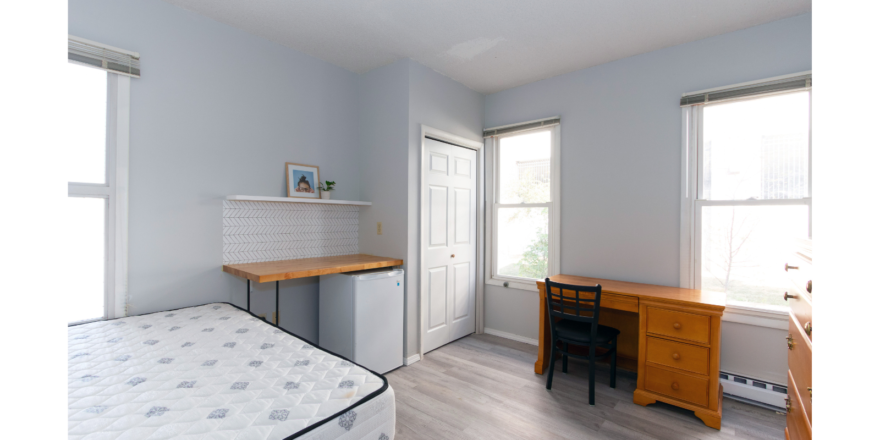 Room with bed, mini-fridge, counter, shelf, desk with chair, and dresser