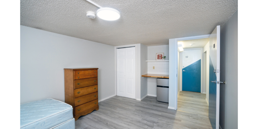 Room with bed, dresser, mini fridge, countertop and shelf