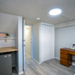 Room with mini-fridge, countertop, shelf, desk, and bed