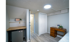 Room with mini-fridge, countertop, shelf, desk, and bed