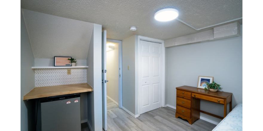 Room with mini-fridge, countertop, shelf, desk, and bed