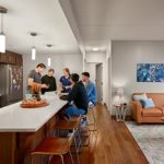 Friends hanging out at a kitchen island next to a decorated living room