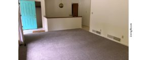 Large, carpeted living room with teal door and pendant light over a stairwell