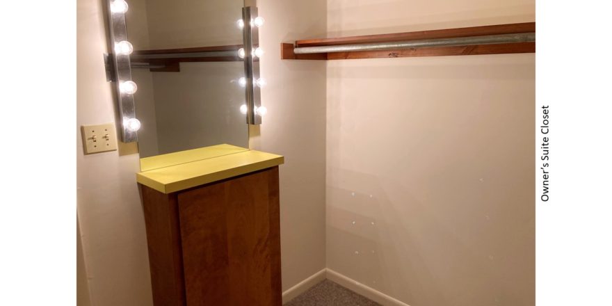 Owner's suite closet with small counter top and mirror with lighting