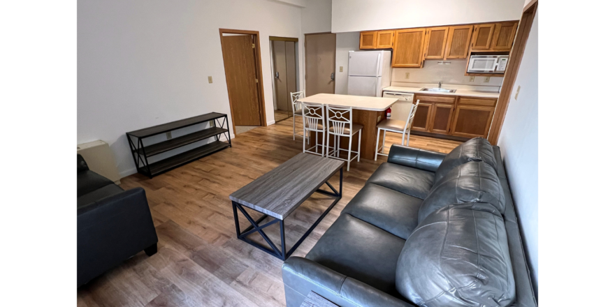 Kitchen with wood-tone cabinets and white appliances, island, and living room with sofa, loveseat, coffee table and TV stand