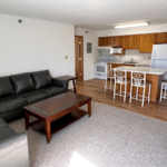 Kitchen with wood-tone cabinets and white appliances, island, and living room with sofa, loveseat, coffee table and end tables