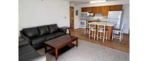 Kitchen with wood-tone cabinets and white appliances, island, and living room with sofa, loveseat, coffee table and end tables