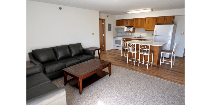 Kitchen with wood-tone cabinets and white appliances, island, and living room with sofa, loveseat, coffee table and end tables