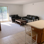 Kitchen with wood-tone cabinets, island, and living room with sofa, loveseat, coffee table, TV stand, and end tables