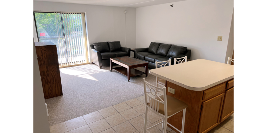 Kitchen with wood-tone cabinets, island, and living room with sofa, loveseat, coffee table, TV stand, and end tables