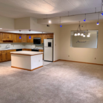 Kitchen with wood-tone cabinets, carpeted living and dining areas, and track lighting