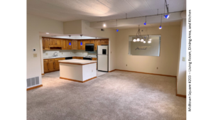 Kitchen with wood-tone cabinets, carpeted living and dining areas, and track lighting