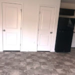 a room with three white doors and a black refrigerator