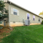 Exterior side of home with pastel green siding, four windows with green shutter trim, large yard, and hvac unit