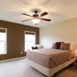 a bedroom with a ceiling fan and two windows