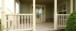 Main entry covered front porch with cream colored railings and hardwood decking. Large ornate front door with a storm door and windows flanking each side