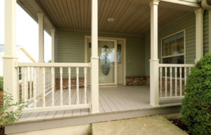 Main entry covered front porch with cream colored railings and hardwood decking. Large ornate front door with a storm door and windows flanking each side