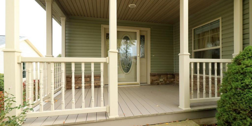 Main entry covered front porch with cream colored railings and hardwood decking. Large ornate front door with a storm door and windows flanking each side