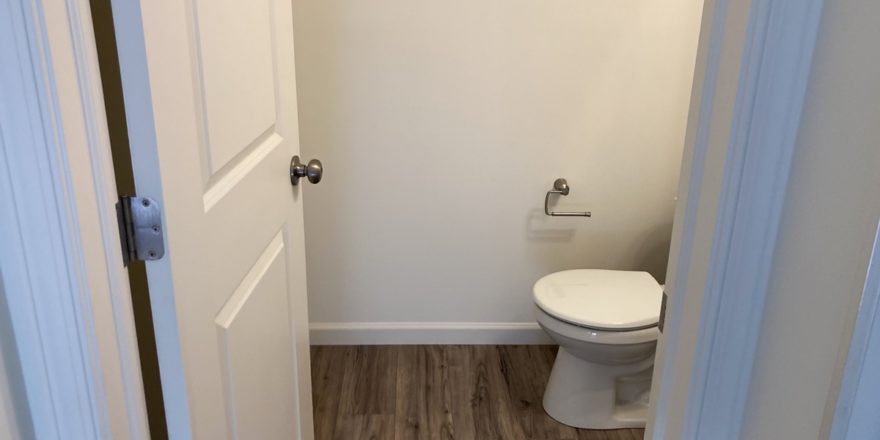 a white toilet in a bathroom on a wooden floor
