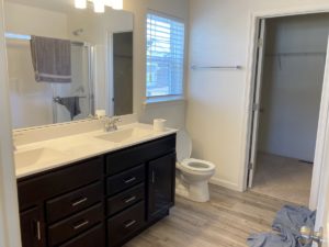 a bathroom with a white toilet, double sink with dark brown cabinets and drawers, a large mirror, and a closet