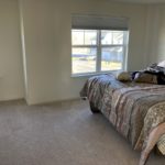 a bedroom with beige carpet, a bed, and two windows