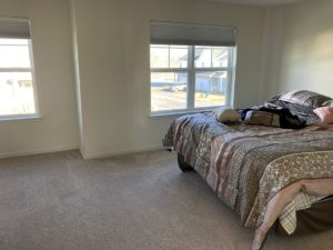 a bedroom with beige carpet, a bed, and two windows