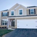 a two story house with tan siding and a two-car garage with a white bay door.