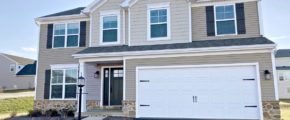 a two story house with tan siding and a two-car garage with a white bay door.