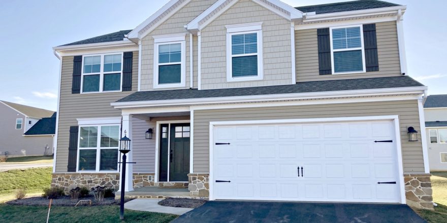 a two story house with tan siding and a two-car garage with a white bay door.