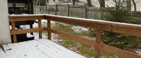 a wooden deck covered in snow with grass below and a wooden fence