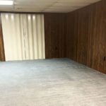 an empty room with wood paneling. beige carpet, a closet with off-white accordion doors and a second closet with off-white bi-fold doors