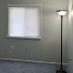 an empty room with light blue carpet, a lamp, and a window