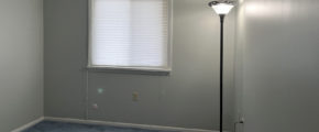 an empty room with light blue carpet, a lamp, and a window