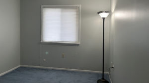 an empty room with light blue carpet, a lamp, and a window