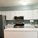 a kitchen with white cabinets, white marbled countertop, and stainless appliances