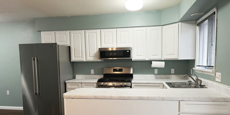 a kitchen with white cabinets, white marbled countertop, and stainless appliances