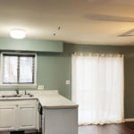 an empty kitchen with white cabinets and wood floors - stainless steel refrigerator on left and dishwasher on right