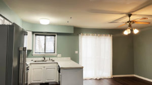 an empty kitchen with white cabinets and wood floors - stainless steel refrigerator on left and dishwasher on right