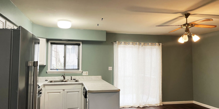 an empty kitchen with white cabinets and wood floors - stainless steel refrigerator on left and dishwasher on right