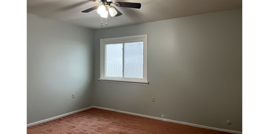 an empty room with a ceiling fan and window