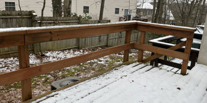 a snow covered back yard, wooden deck, and fence