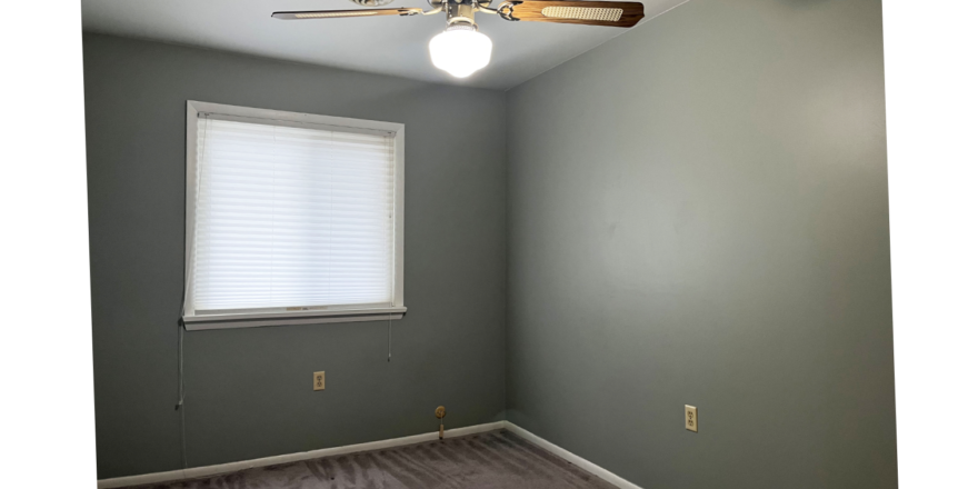 an empty room with light brown carpeting, a ceiling fan, and a window