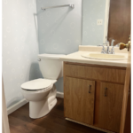 an off-white toilet sitting on dark wood flooring next to an off-white bathroom sink with chrome fixtures and dark wood vanity