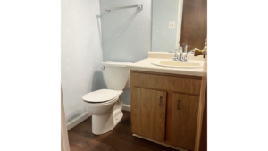 an off-white toilet sitting on dark wood flooring next to an off-white bathroom sink with chrome fixtures and dark wood vanity