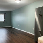 an empty living room with hard wood floors with stainless steel refrigerator in foreground