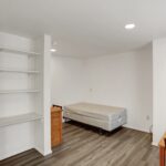an empty room with a bed, desk and shelves